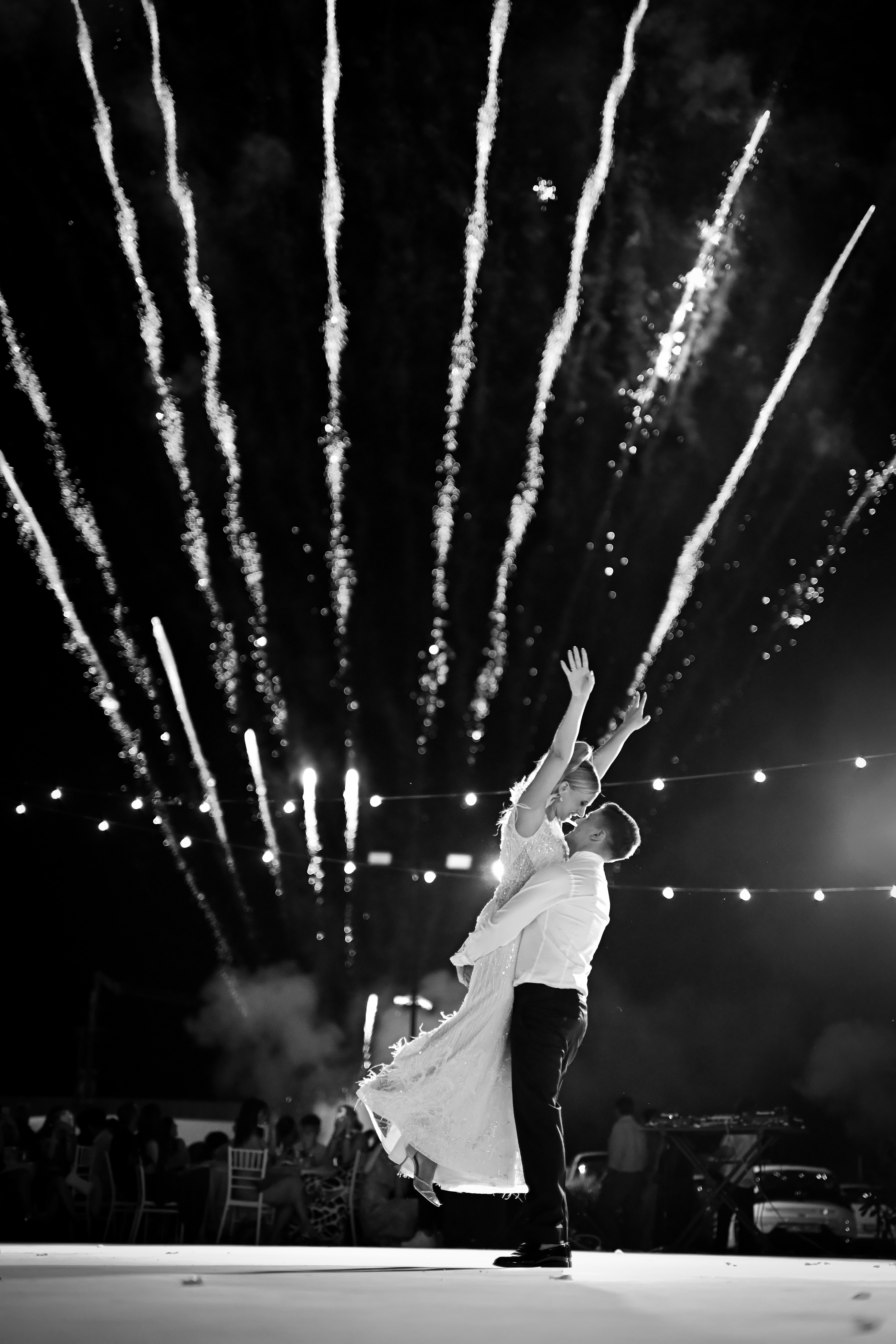 Ασπρόμαυρη φωτογραφία νεόνυμφων χορεύουν κάτω από πυροτεχνήματα - Φωτογραφείο Κολοβός